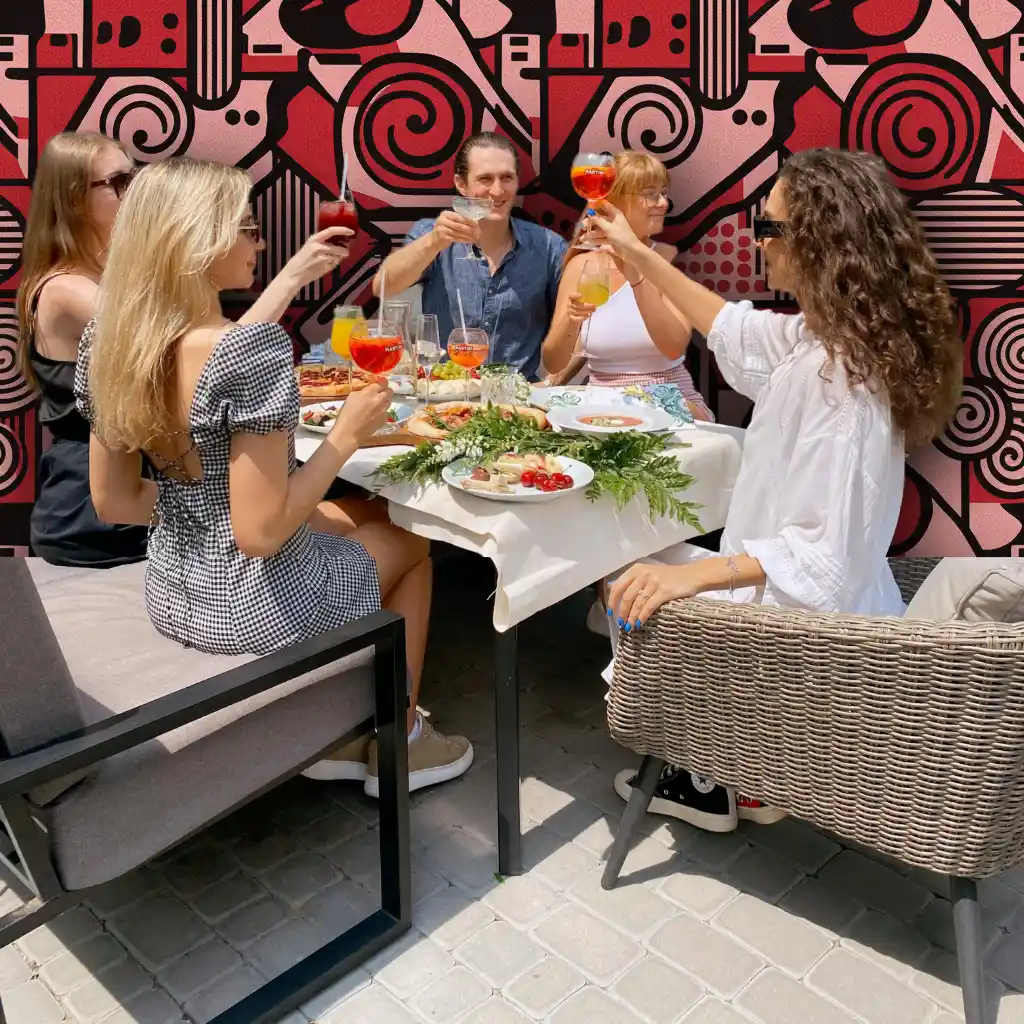 Best Restaurant Website Design Kelowna Friends toast with cocktails on a sunny patio, enjoying pizza & food from a restaurant with a modern red art background